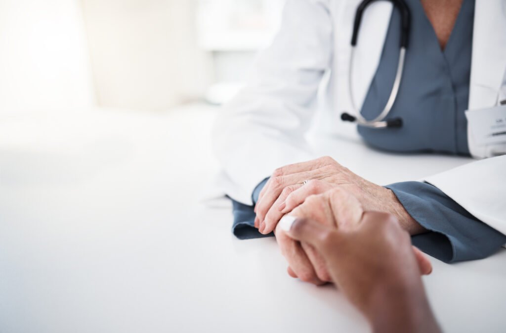A doctor gently holds a patient's hand, conveying support and compassion during a medical consultation.